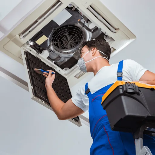 Technician on a ladder inspecting an open ceiling cassette unit