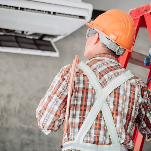 Technician on a ladder connecting pressure gauges to an air conditioner