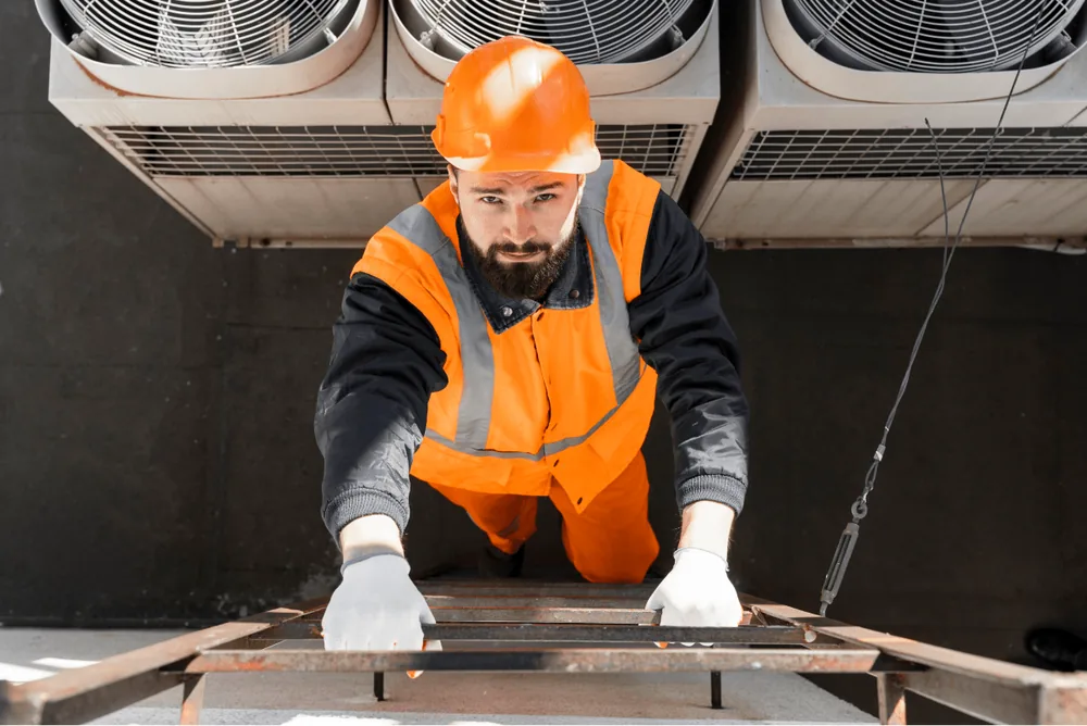 Technician in a hard hat and hi-vis vest working beneath a bank of condenser units