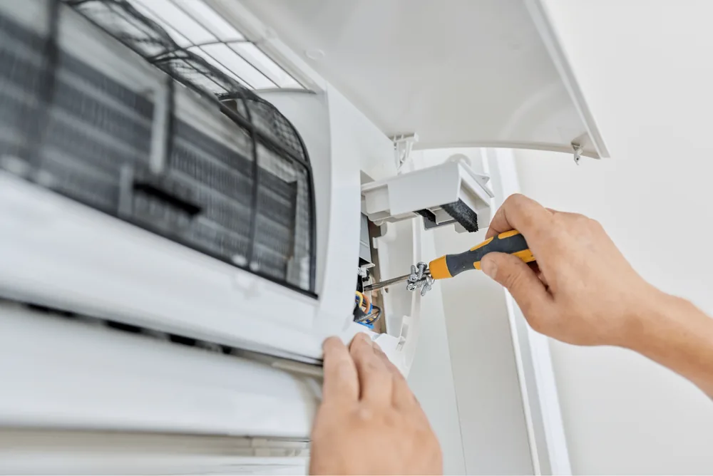 Hands working on the terminal block of an air conditioner with a screwdriver