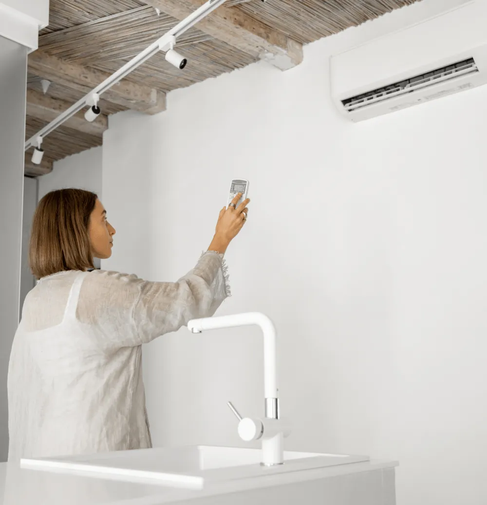 A woman setting a wall-mounted air conditioner with its remote
