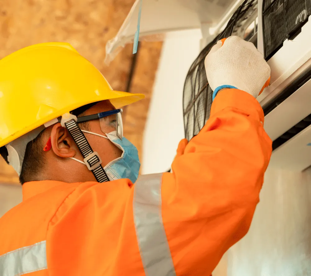 Technician in a hard hat and safety glasses removing the filter from a wall-mounted air conditioner